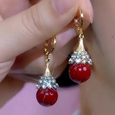 Hand holding pair of gold tone red bead crystal drop dangle earrings