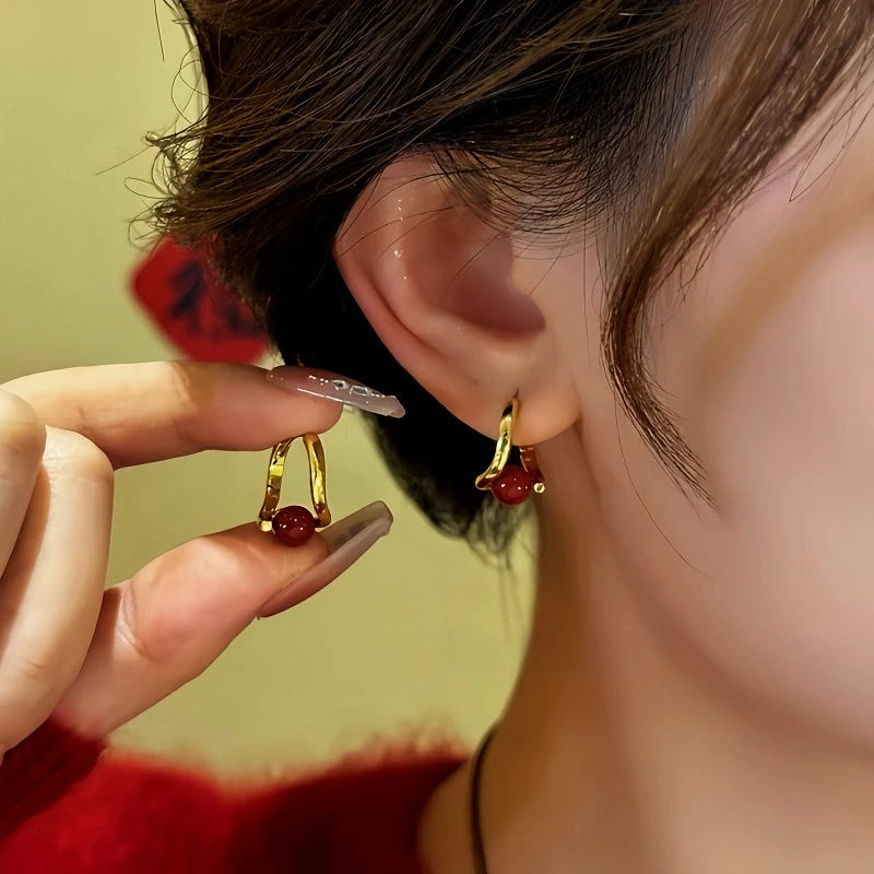 Small gold red bead huggie hoop earrings, hand holding matching pair near ear