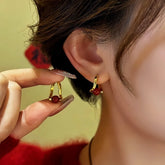 Small gold red bead huggie hoop earrings, hand holding matching pair near ear