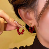 Women's red beaded gold stud C-shaped hoop earrings, hand holding one beside worn earring