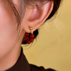 Side angle close-up of red beaded gold stud C-shaped hoop earring on woman's ear