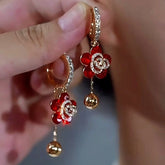 Pair of red crystal flower rhinestone gold ball drop hoop earrings held in hand