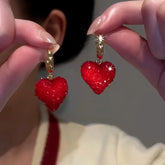 Pair of sparkly red heart gold hoop dangle earrings held in hands