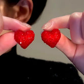 Pair of red sparkly heart stud earrings held between fingers