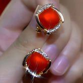 Gold red cushion-cut gemstone stud earrings with crystal accents held in hand