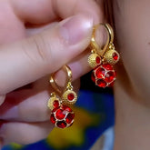 Pair of women's gold red crystal ball dangle hoop earrings held in hand
