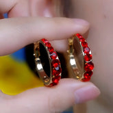 Pair of gold red rhinestone huggie hoop earrings held between fingers, close-up