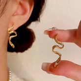 Gold twisted snake drop earring, worn on ear and held by hand