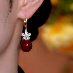 Model showcasing the dangle and style of the 14K Gold-Plated Zircon Flower Red Pearl Earrings