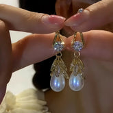Pair of gold leaf teardrop pearl dangle earrings with cubic zirconia, hand-held closeup