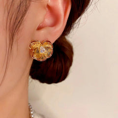 Close-up of gold ridged four-petal flower stud earring with teardrop CZ on a woman's ear