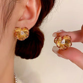 Gold ridged four-petal flower stud earrings with teardrop cubic zirconia, worn and held by hand