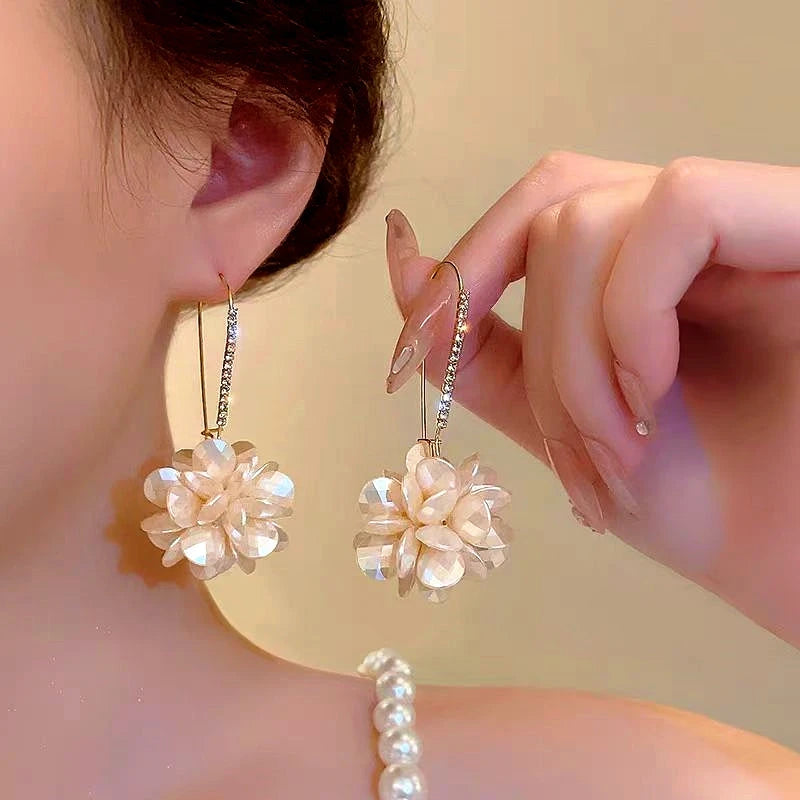 Pearlescent white flower rhinestone hook dangle earrings worn on ear, held by hand