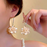 Pearlescent white flower rhinestone hook dangle earrings worn on ear, held by hand