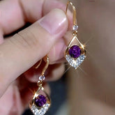 Pair of women's gold purple rose gem crystal drop dangle earrings held in hand