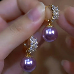 Pair of gold purple pearl drop earrings with crystal leaf accents held in hand