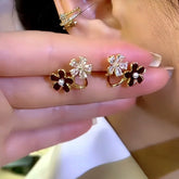 Women's gold dual-flower earring pair: red enamel pearl & clear crystal held in hand