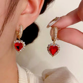 Gold red heart crystal drop hoop earrings, one worn on ear one held by hand
