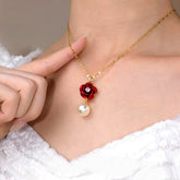 Women's gold necklace with red rose & pearl pendant, hand pointing at detail