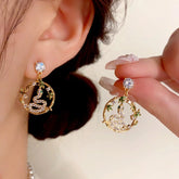 Gold bamboo snake CZ dangle earrings: one worn on ear, one held by hand