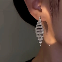 Silver tiered crystal drop earring worn on ear in warm light