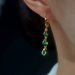 Gold emerald green teardrop dangle hoop earring worn on ear close-up