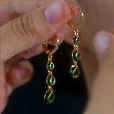 Hand holding pair of gold emerald green teardrop dangle hoop earrings