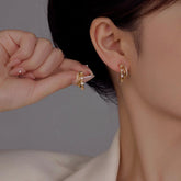 Gold triple-layer CZ hoop stud earrings worn on woman's ear, hand holding matching earring