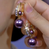 Pair of gold crystal purple pearl drop earrings held in hand