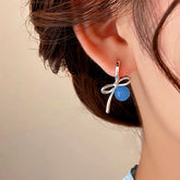 Women's silver bow blue stone dangle huggie earring worn on ear, close-up