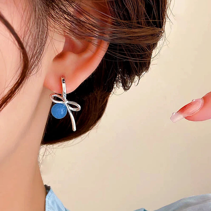 Model showcasing the dangle and style of the 14K Gold-plated Bow Bead Blue Bead Earrings