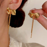 Gold bow chain tassel dangle earrings, one worn on ear, one held in hand