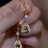 Pair of gold champagne teardrop crystal drop earrings held in hand