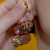 Pair of rose gold amber crystal round drop earrings with clear accent held in hand