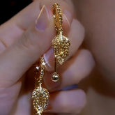 Pair of sparkly gold leaf dangle hoop earrings held in hand