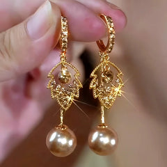 Pair of gold leaf crystal champagne pearl drop hoop earrings held in hand