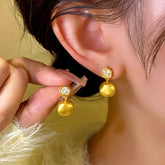 Women's brushed gold cushion drop earrings with clear gem, hand held next to worn earring