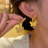 Gold butterfly huggie hoop earrings with tiny crystal drop, held beside worn earring