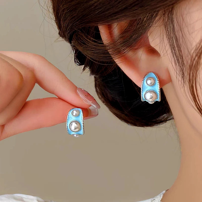 Vintage women's light blue enamel silver pearl stud earrings, one worn on ear, one held by hand
