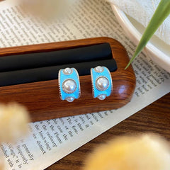 Silver tone light blue enamel pearl C-hoop earrings on wooden jewelry display