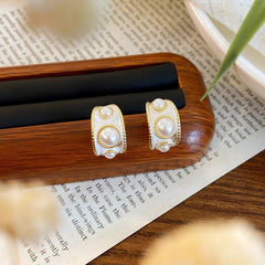 Pair of vintage women's white enamel gold pearl stud earrings on wooden stand over book page