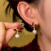Burgundy enamel flower pearl drop earrings worn on ear, matching piece held for detail