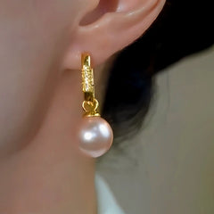 Gold pave pearl drop huggie hoop earring worn on a person's ear