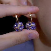 Pair of purple crystal ball gold hoop earrings held between fingers