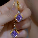 Pair of gold purple square crystal drop dangle earrings held in hand