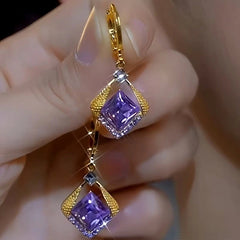 Pair of gold purple square crystal drop dangle earrings held in hand