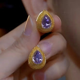 Textured gold teardrop purple gemstone stud earrings held between fingers, close-up
