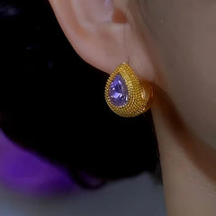 Textured gold teardrop purple gemstone stud earring worn on ear, side close-up