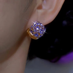 Sparkly purple crystal gold huggie earring worn on woman's earlobe