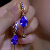 Pair of purple teardrop crystal gold ball dangle hoop earrings held in hand
